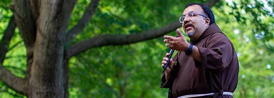 Br. Vito Martinez holds a microphone and speaks outdoors